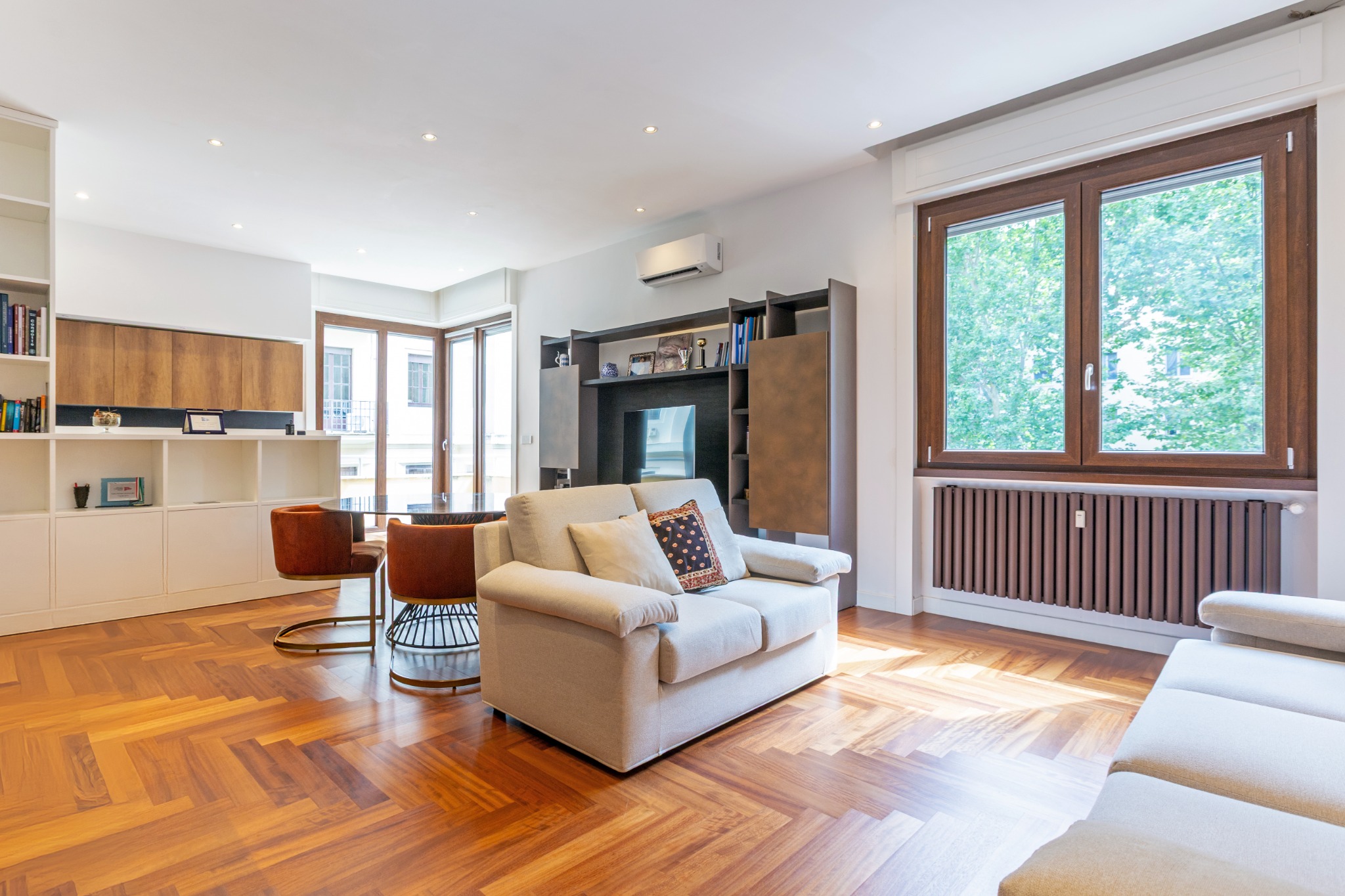 Vista del living luminoso con cucina a vista, parquet a spina di pesce e affacci sul verde
