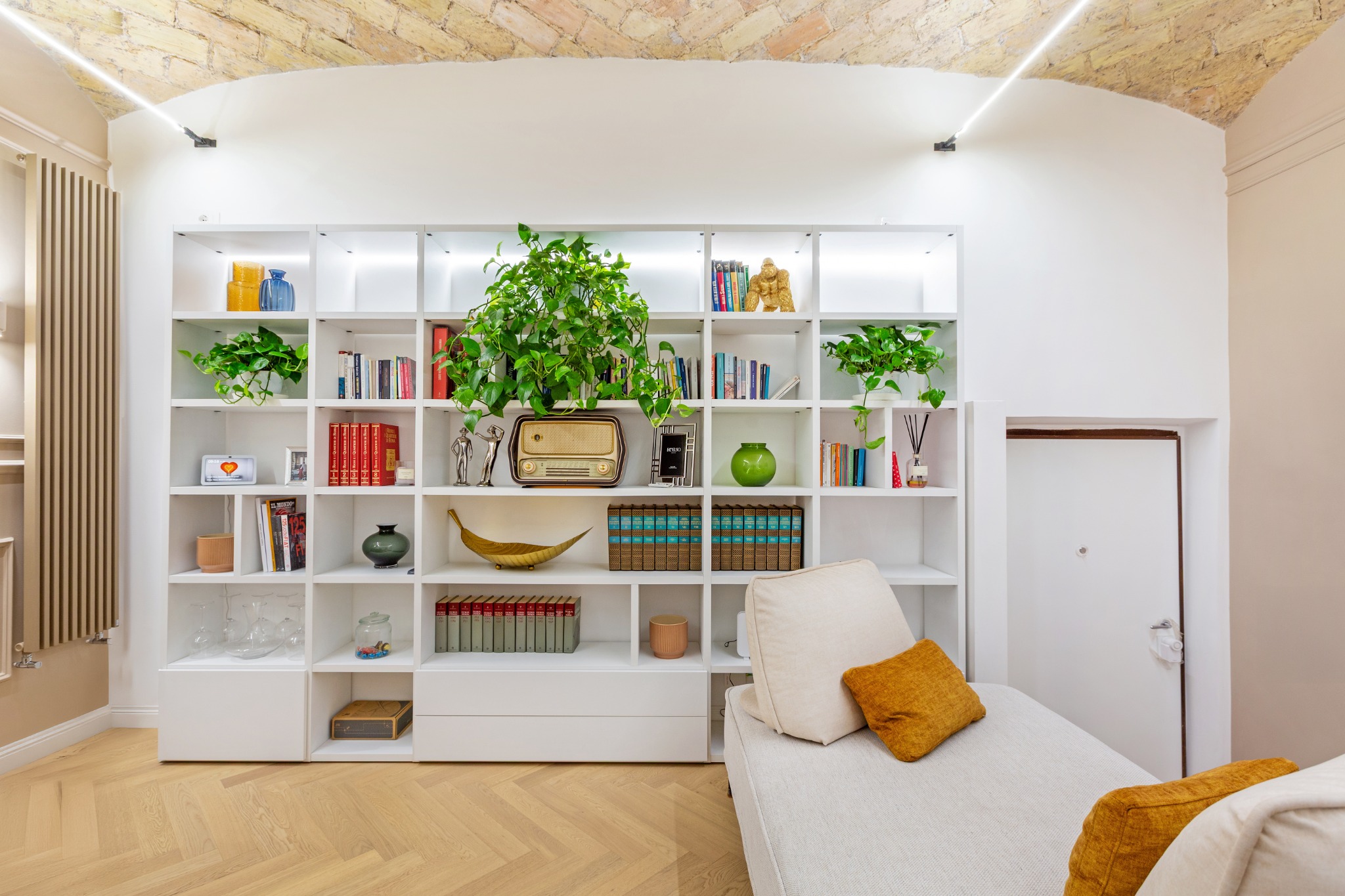 Libreria bianca su misura, divano e soffitto a volta in mattoncini a vista
